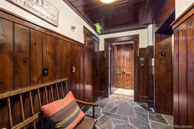interior space featuring wainscoting, wooden walls, wooden ceiling, and stone flooring