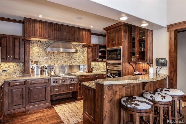 kitchen with a breakfast bar area, range hood, appliances with stainless steel finishes, and tasteful backsplash