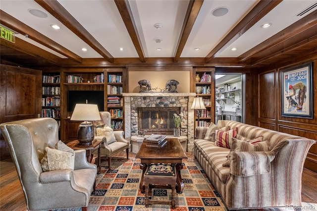 living area with wood finished floors, visible vents, beamed ceiling, a fireplace, and built in features