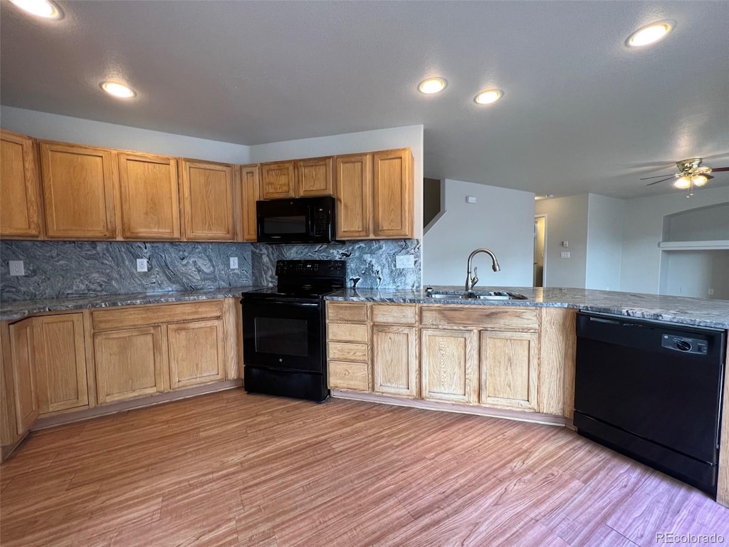 kitchen with sink, light hardwood / wood-style flooring, dark stone countertops, black appliances, and decorative backsplash