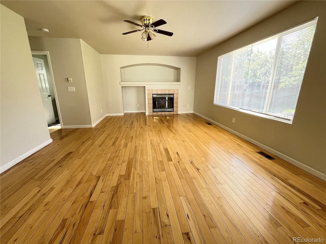 20558 E Grand Ln, Aurora, CO 80015 - unfurnished living room featuring a ceiling fan, a tiled fireplace, light wood-style floors, and baseboards