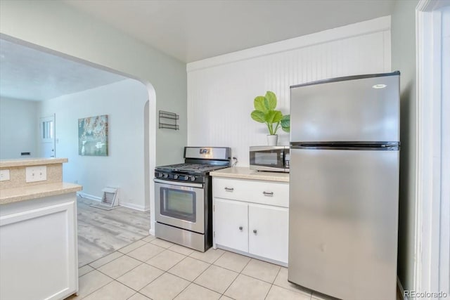 2684 S Logan St, Denver, CO 80210 - kitchen with stainless steel appliances, white cabinetry, light countertops, arched walkways, and light tile patterned floors