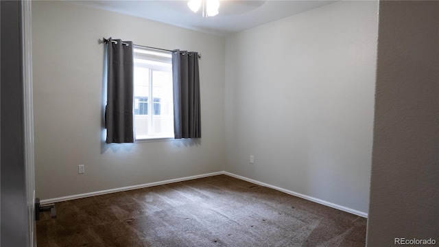 spare room with baseboards, dark colored carpet, and a ceiling fan