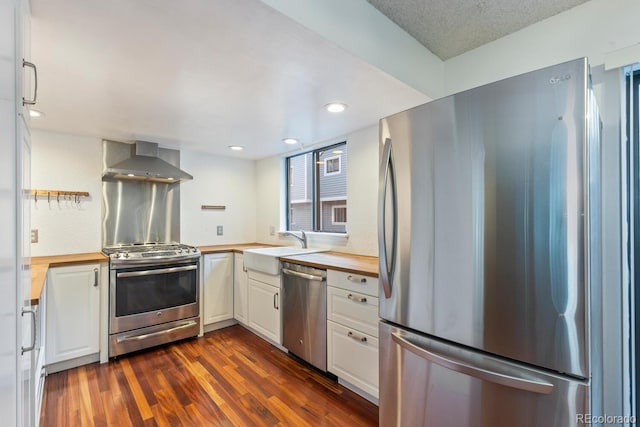 kitchen featuring dark hardwood / wood-style floors, stainless steel appliances, white cabinets, butcher block countertops, and wall chimney range hood