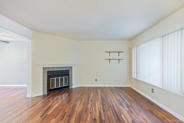 unfurnished living room with dark wood-type flooring, a textured ceiling, and a tiled fireplace