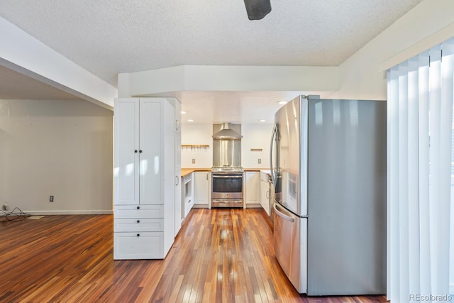 kitchen featuring wall chimney exhaust hood, light hardwood / wood-style flooring, white cabinets, appliances with stainless steel finishes, and a textured ceiling