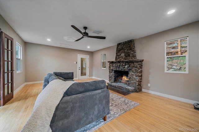 living area with ceiling fan, a stone fireplace, visible vents, baseboards, and wood-type flooring