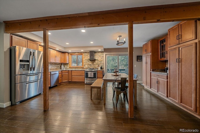 kitchen with backsplash, appliances with stainless steel finishes, brown cabinetry, and wall chimney exhaust hood