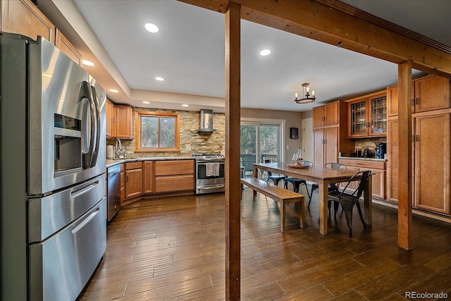 kitchen featuring wall chimney range hood, stainless steel appliances, brown cabinetry, and backsplash