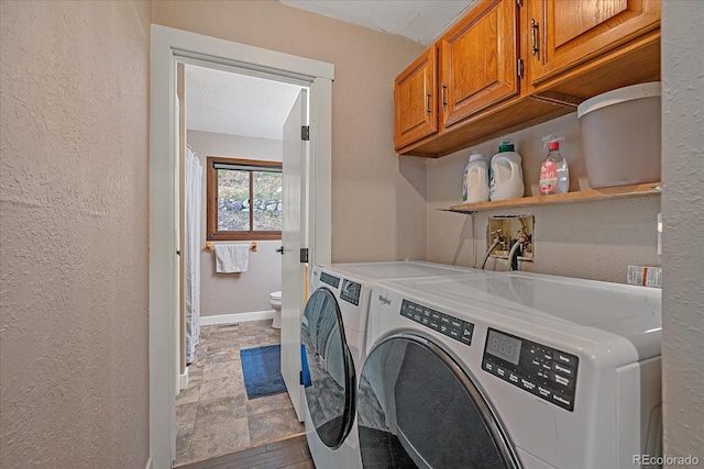 washroom featuring a textured wall, washer and dryer, baseboards, stone finish floor, and cabinet space