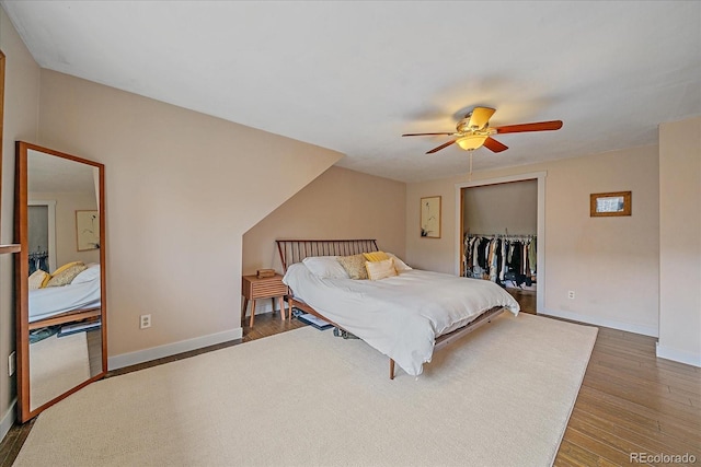 bedroom featuring a ceiling fan, baseboards, wood finished floors, a spacious closet, and a closet