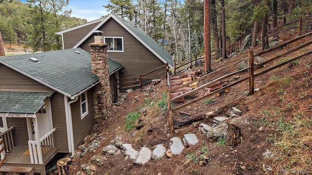 view of side of home featuring roof with shingles, fence, and a deck