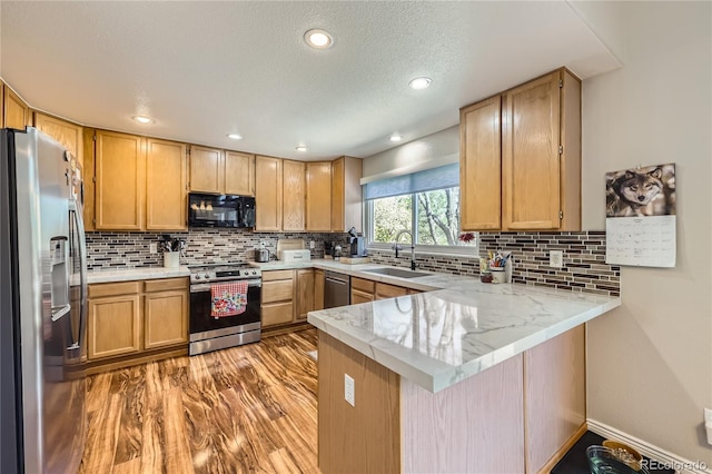 kitchen featuring a peninsula, a sink, appliances with stainless steel finishes, tasteful backsplash, and recessed lighting