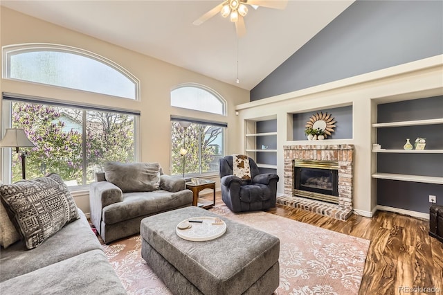 living room with wood finished floors, high vaulted ceiling, a fireplace, ceiling fan, and built in shelves