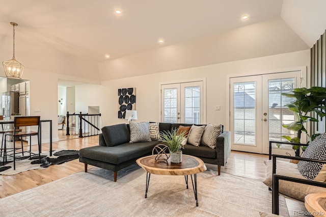 living room with a notable chandelier, vaulted ceiling, light hardwood / wood-style floors, and french doors