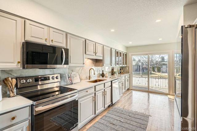 kitchen featuring sink, light wood-type flooring, backsplash, stainless steel appliances, and a textured ceiling