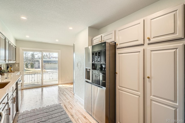 kitchen featuring white cabinets, appliances with stainless steel finishes, a textured ceiling, and light wood-type flooring