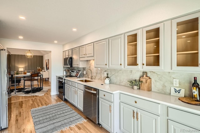 kitchen with tasteful backsplash, stainless steel appliances, sink, and light wood-type flooring