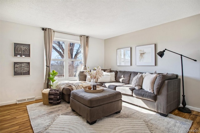 living area featuring a textured ceiling, wood finished floors, visible vents, and baseboards