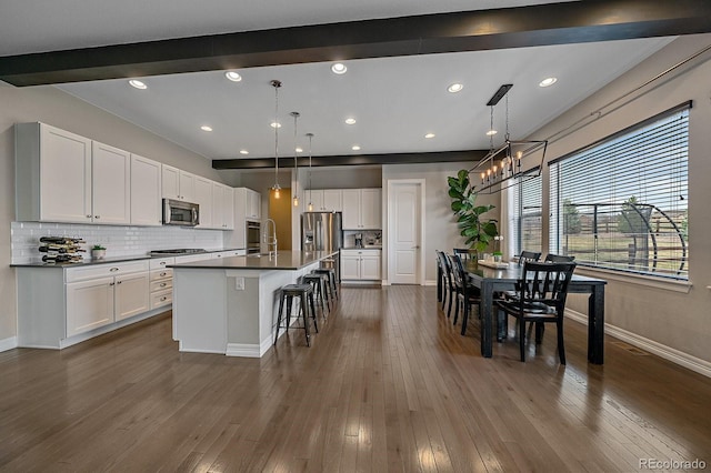 14589 Hagus Pl, Parker, CO 80134 - kitchen with stainless steel appliances, dark countertops, a chandelier, white cabinetry, and a breakfast bar