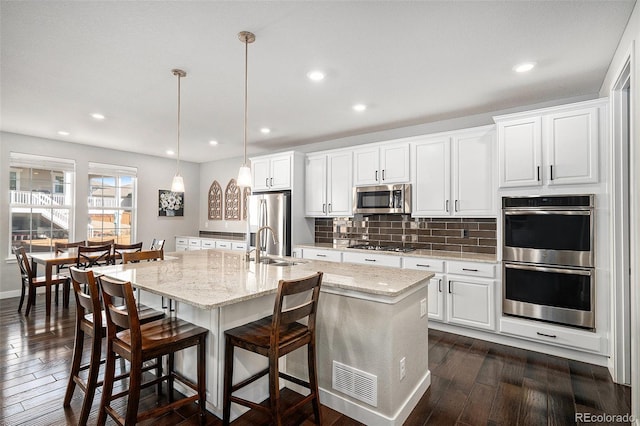 kitchen featuring dark wood-style floors, a center island with sink, white cabinets, appliances with stainless steel finishes, and tasteful backsplash