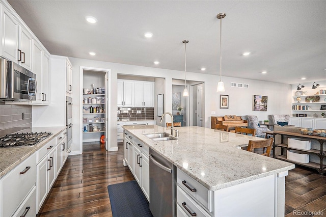 kitchen with dark wood finished floors, open floor plan, stainless steel appliances, white cabinetry, and a sink