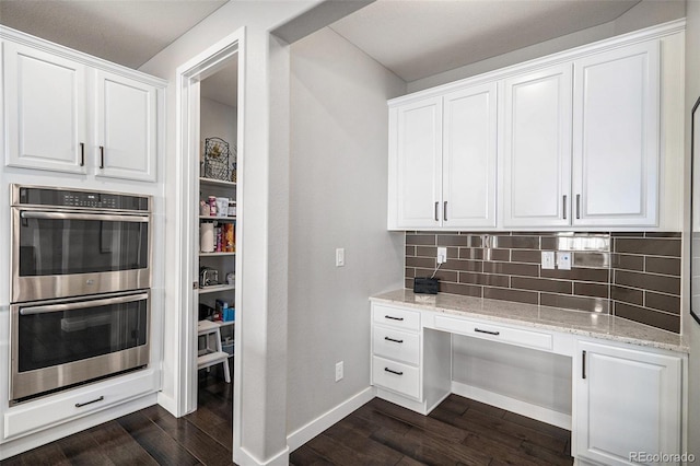 kitchen with stainless steel double oven, tasteful backsplash, dark wood-type flooring, and white cabinetry