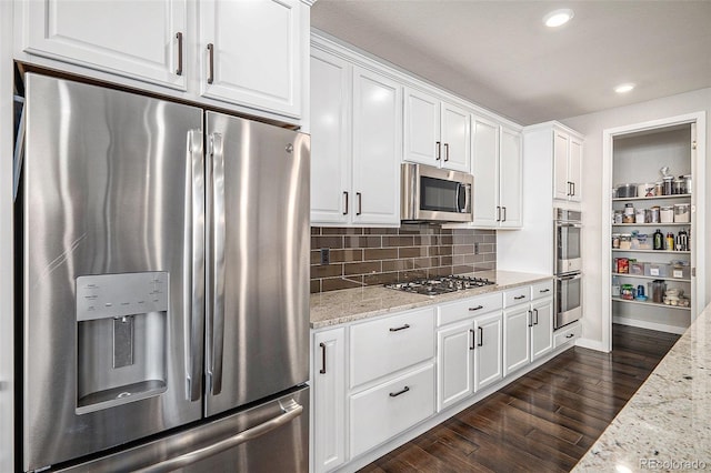 kitchen with light stone countertops, dark wood finished floors, decorative backsplash, appliances with stainless steel finishes, and white cabinetry