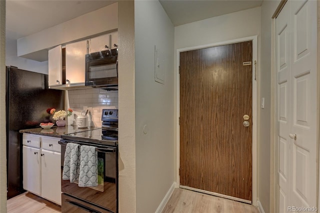 kitchen featuring light wood finished floors, white cabinets, dark stone countertops, black appliances, and backsplash