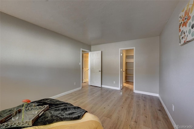 bedroom with a spacious closet, light wood-type flooring, and baseboards