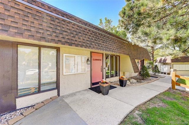 property entrance with stucco siding, mansard roof, and roof with shingles