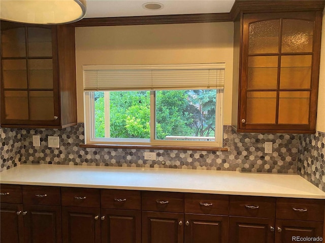 kitchen featuring decorative backsplash, light countertops, glass insert cabinets, and dark brown cabinetry
