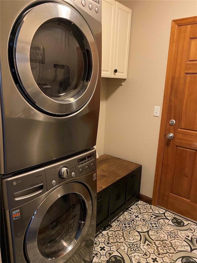 laundry room featuring stacked washer and dryer, baseboards, cabinet space, and light tile patterned flooring