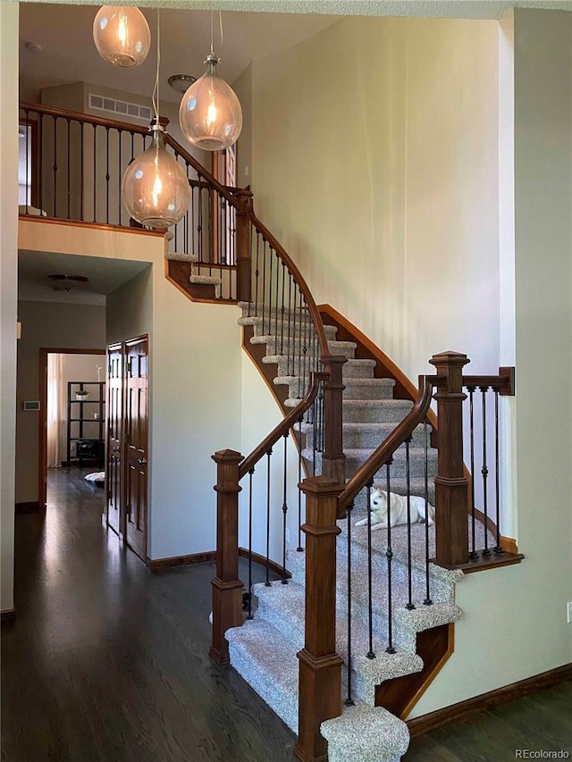 staircase with a high ceiling, baseboards, visible vents, and wood finished floors