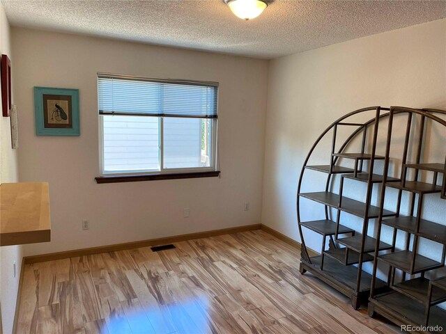 bedroom with light wood-type flooring, baseboards, visible vents, and a textured ceiling
