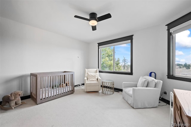 carpeted bedroom featuring a nursery area, ceiling fan, and baseboards