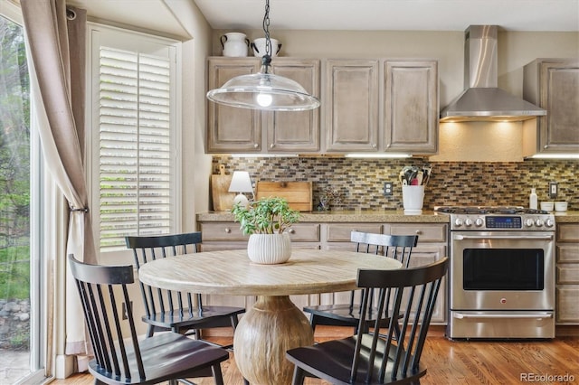 kitchen with wall chimney range hood, tasteful backsplash, stainless steel range with gas stovetop, light wood-type flooring, and light countertops