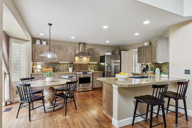 kitchen featuring a sink, a peninsula, wall chimney range hood, visible vents, and appliances with stainless steel finishes
