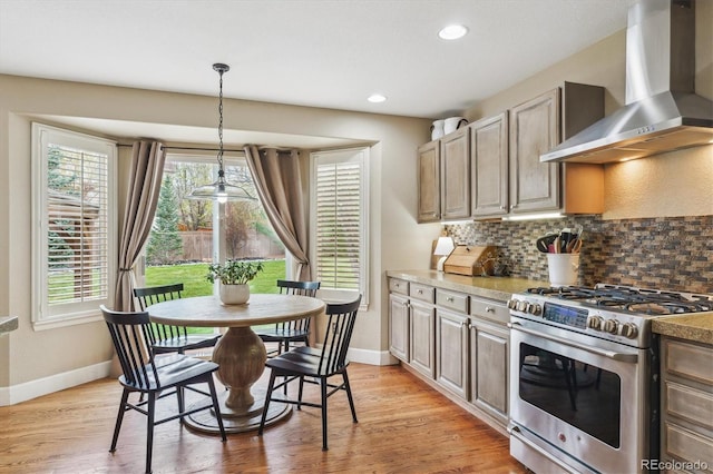 kitchen with baseboards, wall chimney exhaust hood, stainless steel range with gas cooktop, tasteful backsplash, and light wood-type flooring