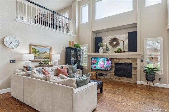 living area featuring a towering ceiling, baseboards, a stone fireplace, and wood finished floors