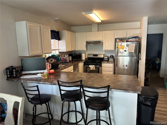 kitchen with a kitchen bar, kitchen peninsula, dark hardwood / wood-style floors, and stainless steel appliances