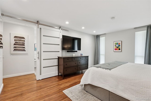 bedroom with recessed lighting, baseboards, a barn door, and light wood-style floors