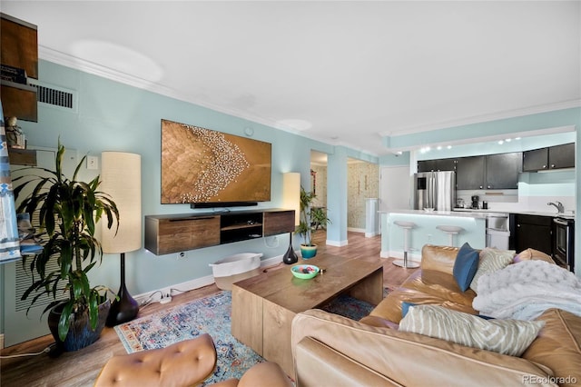 living room featuring baseboards, ornamental molding, visible vents, and light wood-style floors