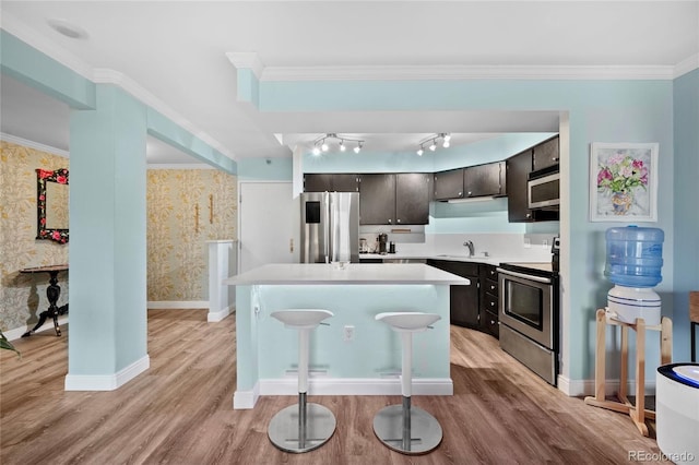 kitchen featuring a center island, light countertops, appliances with stainless steel finishes, a sink, and wallpapered walls