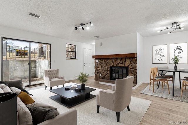 living room with a stone fireplace, light wood-style flooring, visible vents, and a textured ceiling