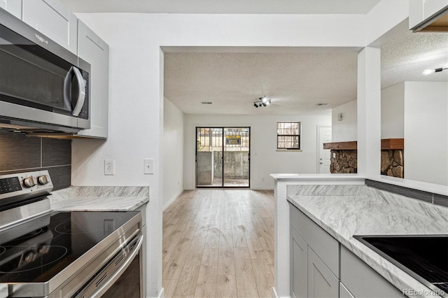 kitchen with baseboards, light wood-style flooring, stainless steel appliances, a textured ceiling, and open floor plan