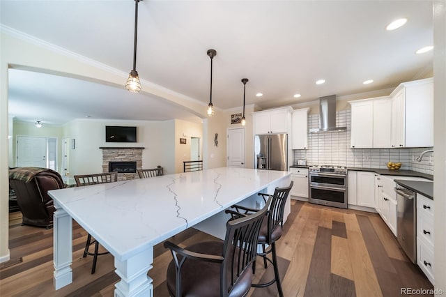 kitchen with white cabinets, decorative light fixtures, high end appliances, and wall chimney exhaust hood