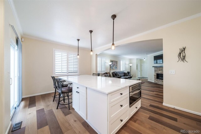 kitchen with a stone fireplace, dark hardwood / wood-style floors, decorative light fixtures, light stone counters, and white cabinetry