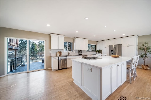 kitchen featuring a sink, white cabinets, appliances with stainless steel finishes, light wood-type flooring, and a center island