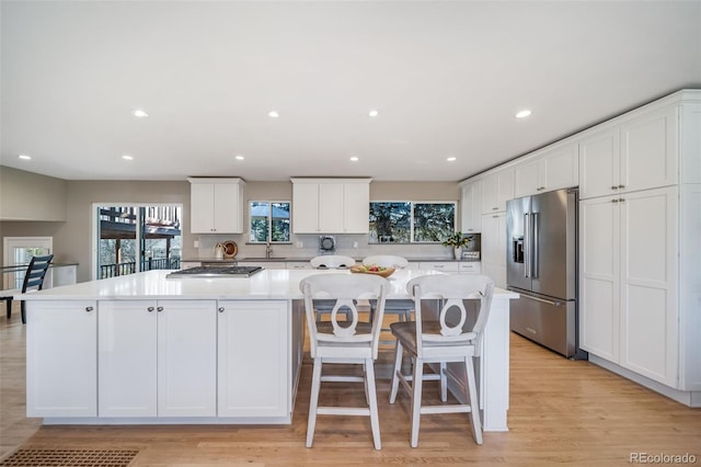 kitchen featuring light wood-type flooring, light countertops, high quality fridge, a large island, and white cabinets